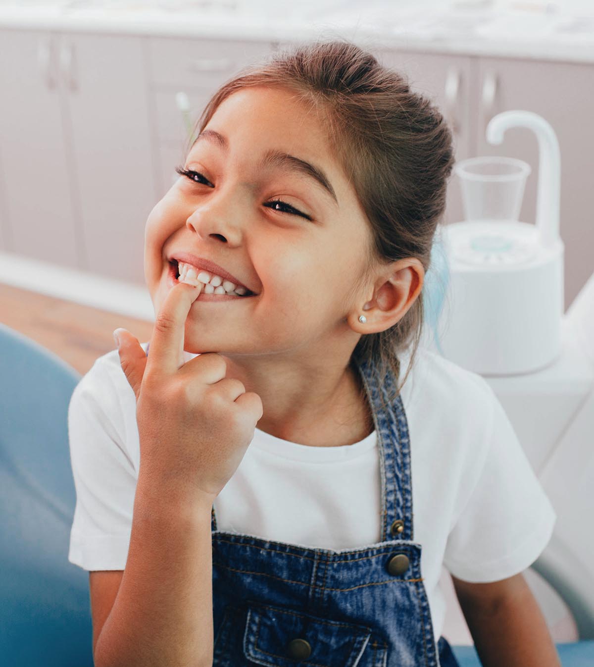 Mixed race little patient showing her perfect toothy smile while sitting dentists chair