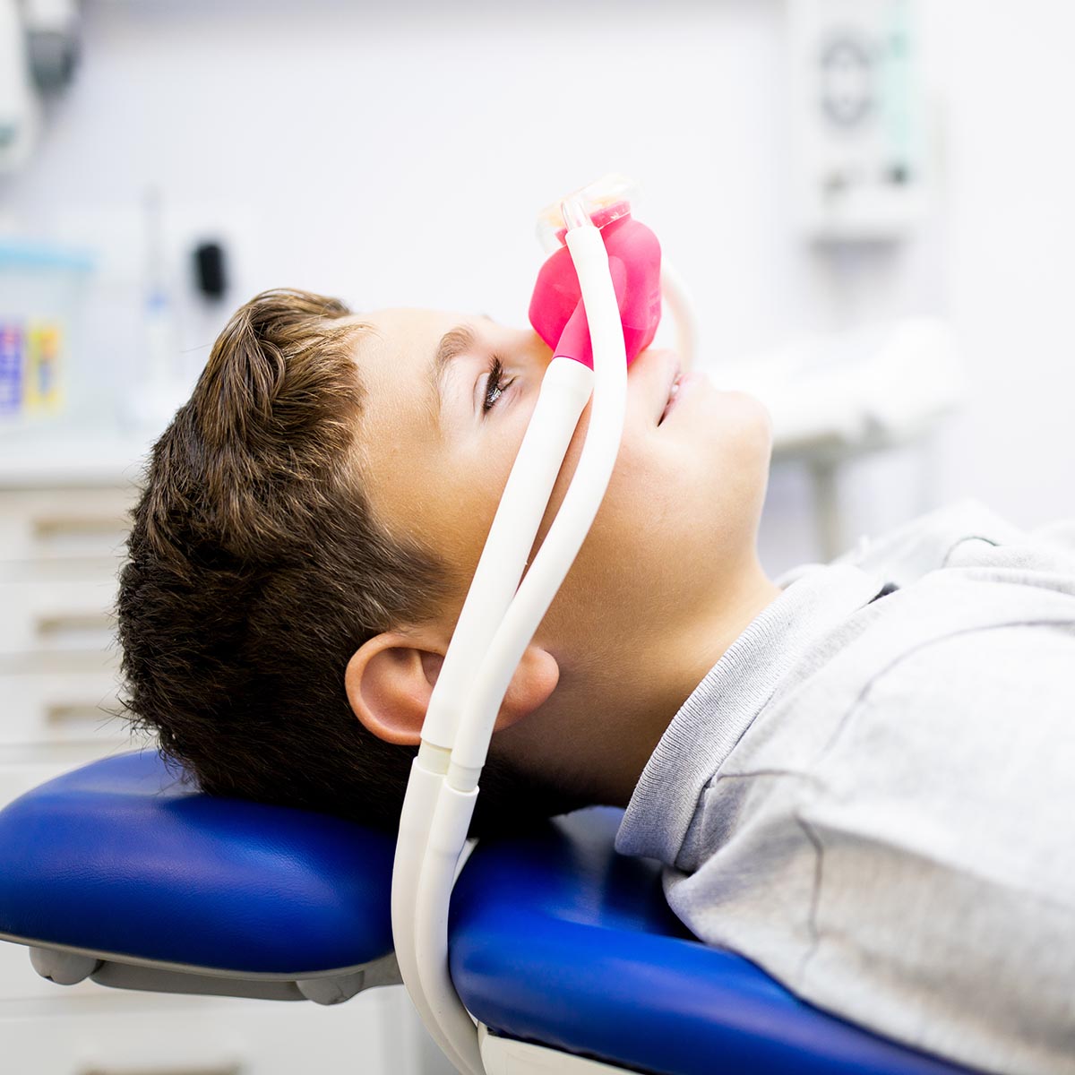 Fear of the dentist! A little boy sits in a dentist's office wearing a nasal mask breathing nitrous oxide to relax.Concept of feeling relaxed with laughing gas.Anxiety about visiting a dentist.